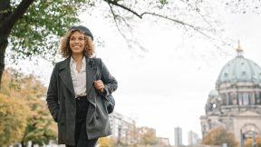 Student walks through the city smiling with the Berlin Cathedral in the background.