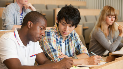 Internationale Studierende sitzen über Studienmaterialien im Hörsaal.