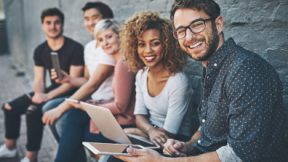 Internationale Alumni sitzen auf einer Bank an der Universität und lächeln in die Kamera.