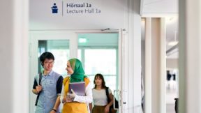 Two students are talking in the corridor outside the lecture hall.