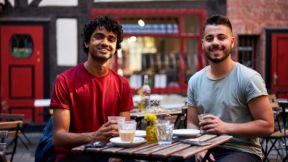 Two students sit smiling outside at a table in the café.