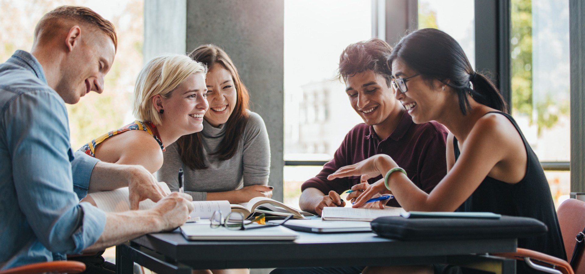 International students sit laughing at a table in the university and study together.