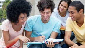 A group of multi-ethnic students study outdoors on campus in the summer.